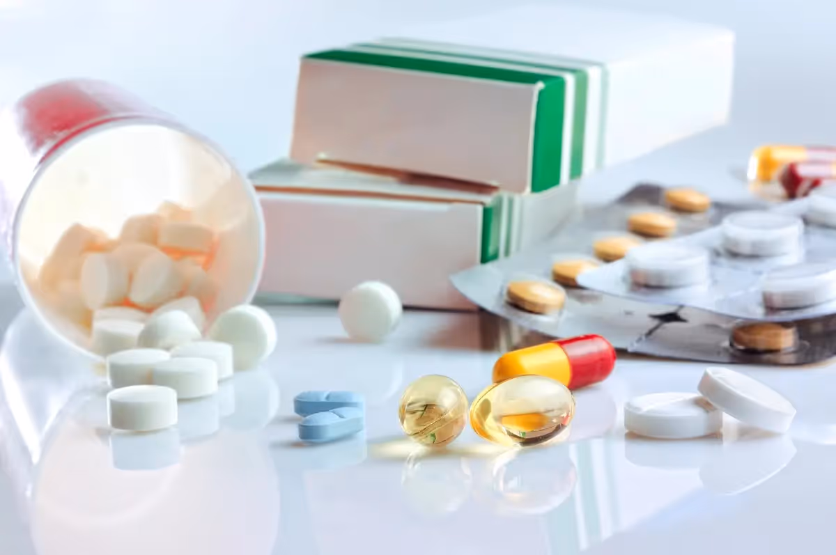 Cajas, blísters y comprimidos de medicamentos sobre una superficie blanca, ilustrando la adecuación de los formatos de antibióticos de la AEMPS